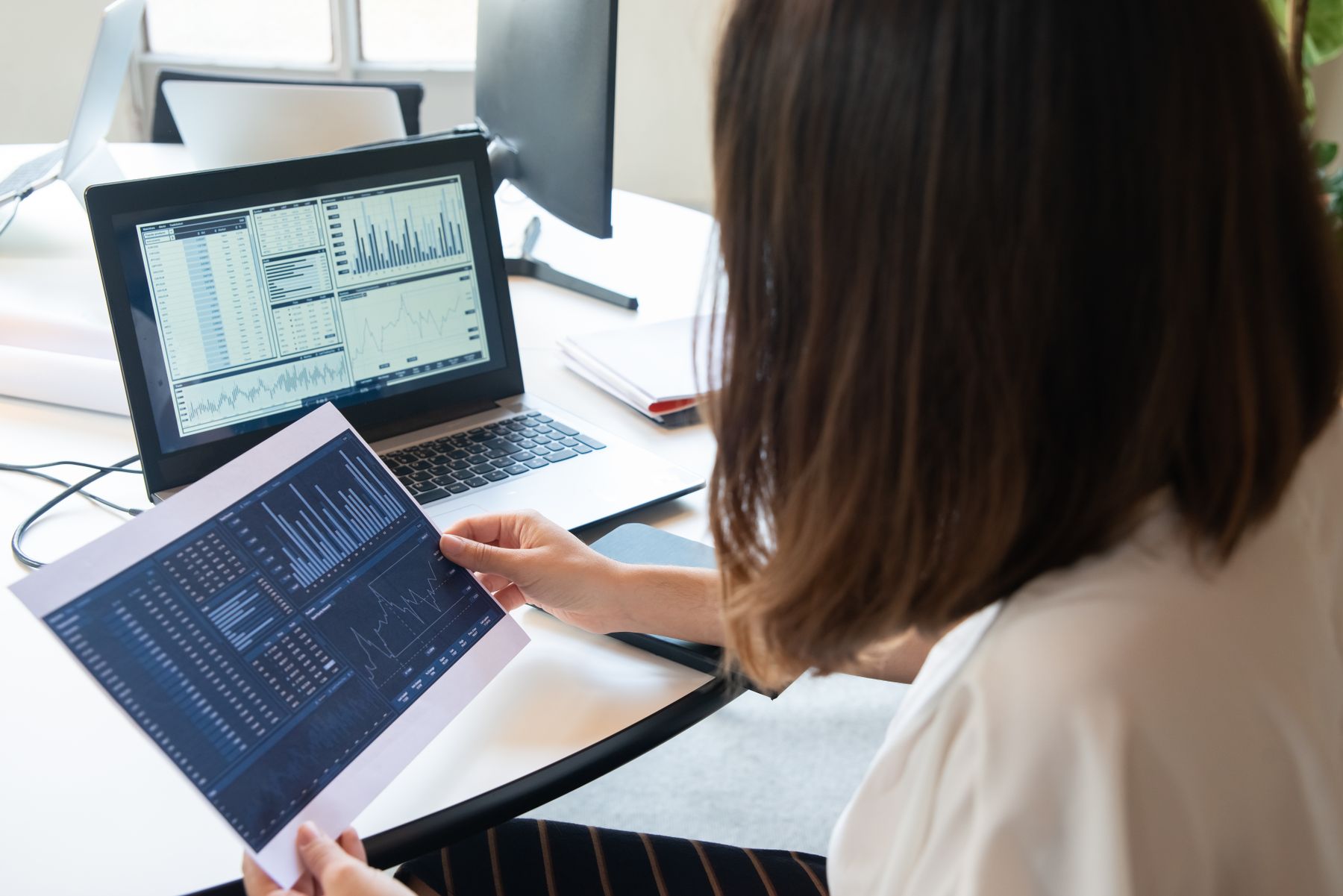 Financial analyst reviewing company reports and charts beside a laptop